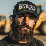 Bearded man wearing Killdozer trucker hat outdoors near heavy machinery
